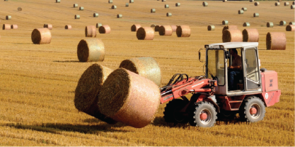 A tractor picks of bales of hay in a field.