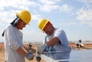 Two construction workers wear wide-brimmed hard hats. One wears a neck cover.